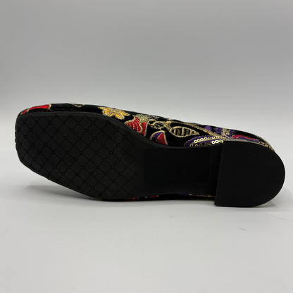 A single black leather shoe shown from the sole side, featuring a black textured rubber outsole with a detailed embroidery pattern and a black heel. The upper is decorated with vibrant multicolor embroidery in red, gold, and purple tones.