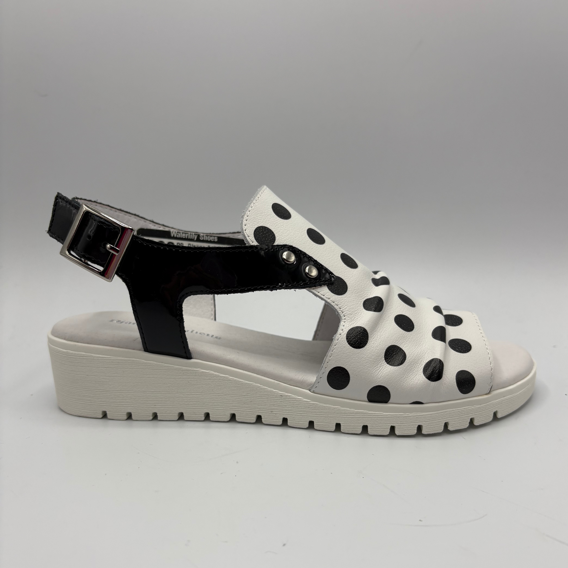 White sandal with black polka dots and a black strap on a gray background