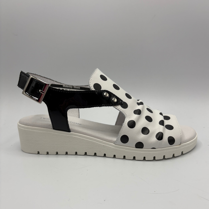 White sandal with black polka dots and a black strap on a gray background