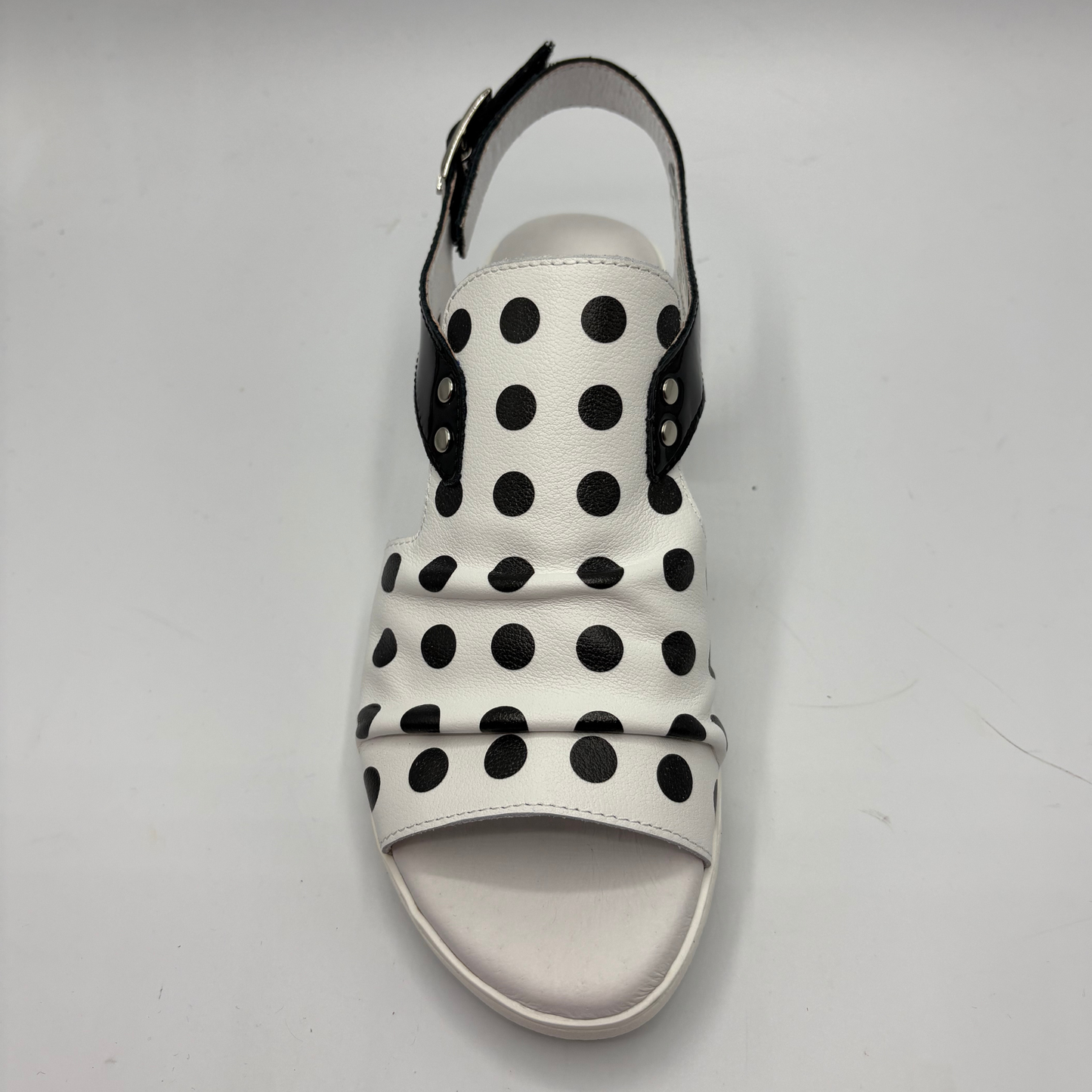 White sandal with black polka dots on a light gray background