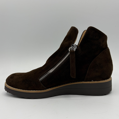 A dark brown suede ankle boot with a side zipper, a pull tab, and a wedge heel, shown in profile against a light gray background.