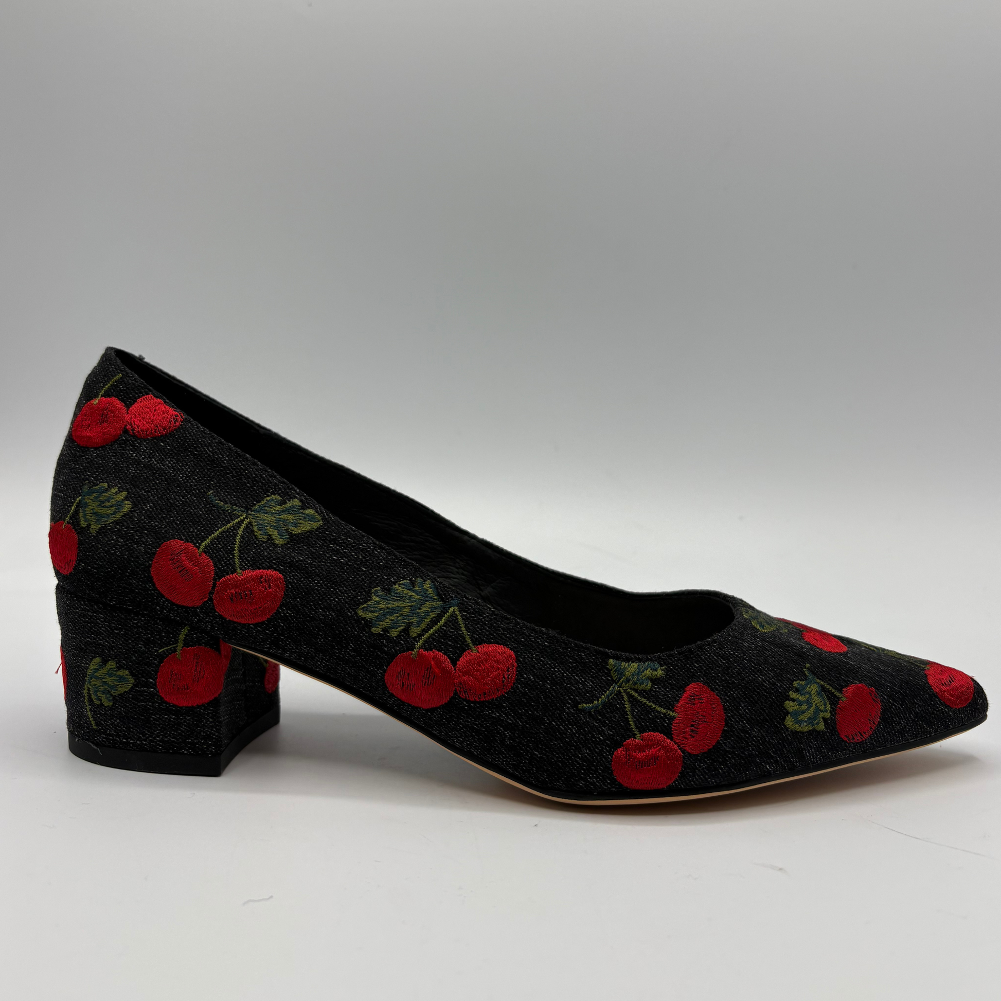 A black pointed-toe pump with a block heel, featuring an embroidered pattern of red cherries with green leaves on the upper and heel.