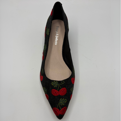 A single pointed-toe flat shoe by Django & Juliette, featuring a black fabric upper with a red cherry and green leaf pattern, photographed from a top-down angle on a light gray background.