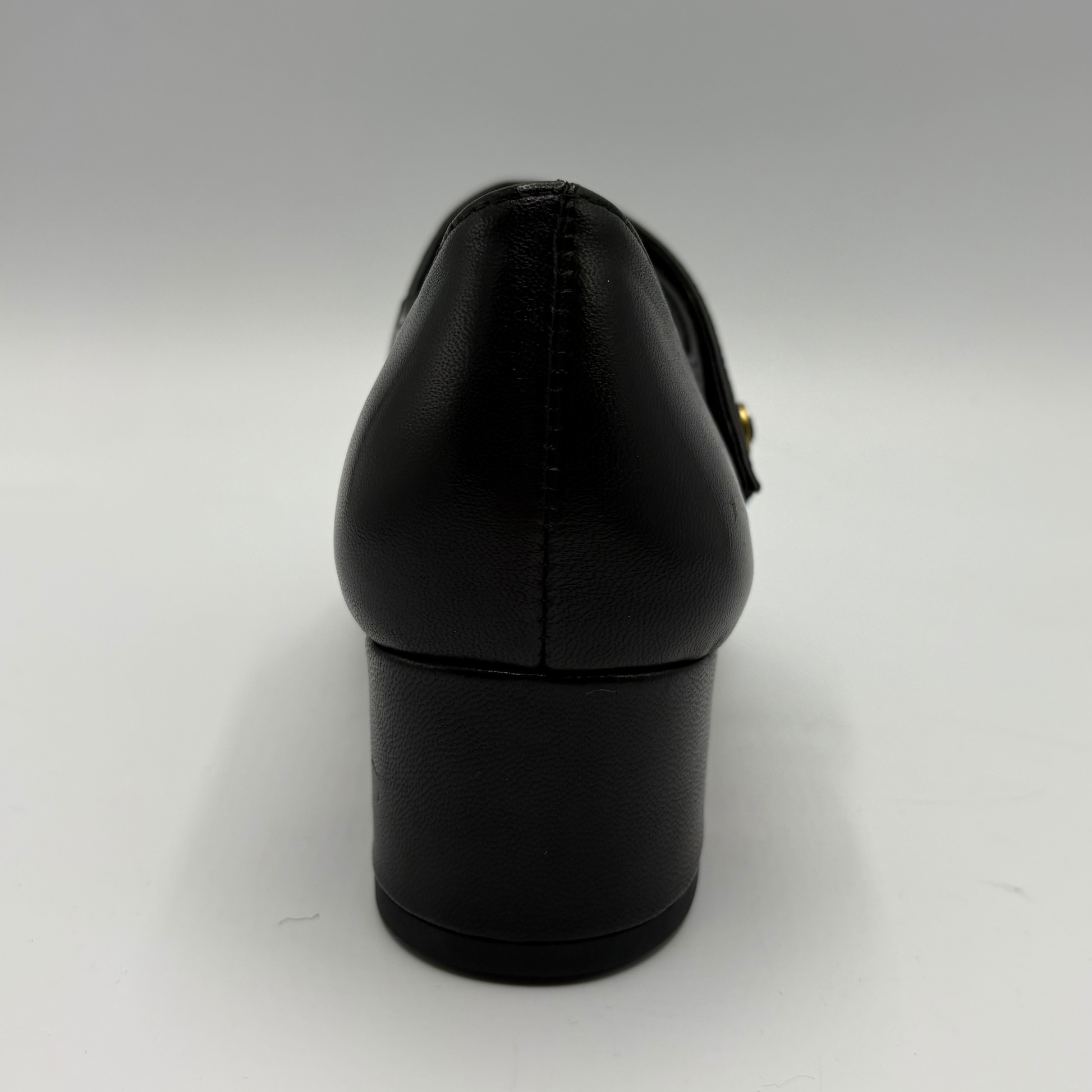A black leather pump shoe shown from a rear three-quarter view, featuring a block heel and a small gold-tone decorative accent on the side, set against a plain light gray background.