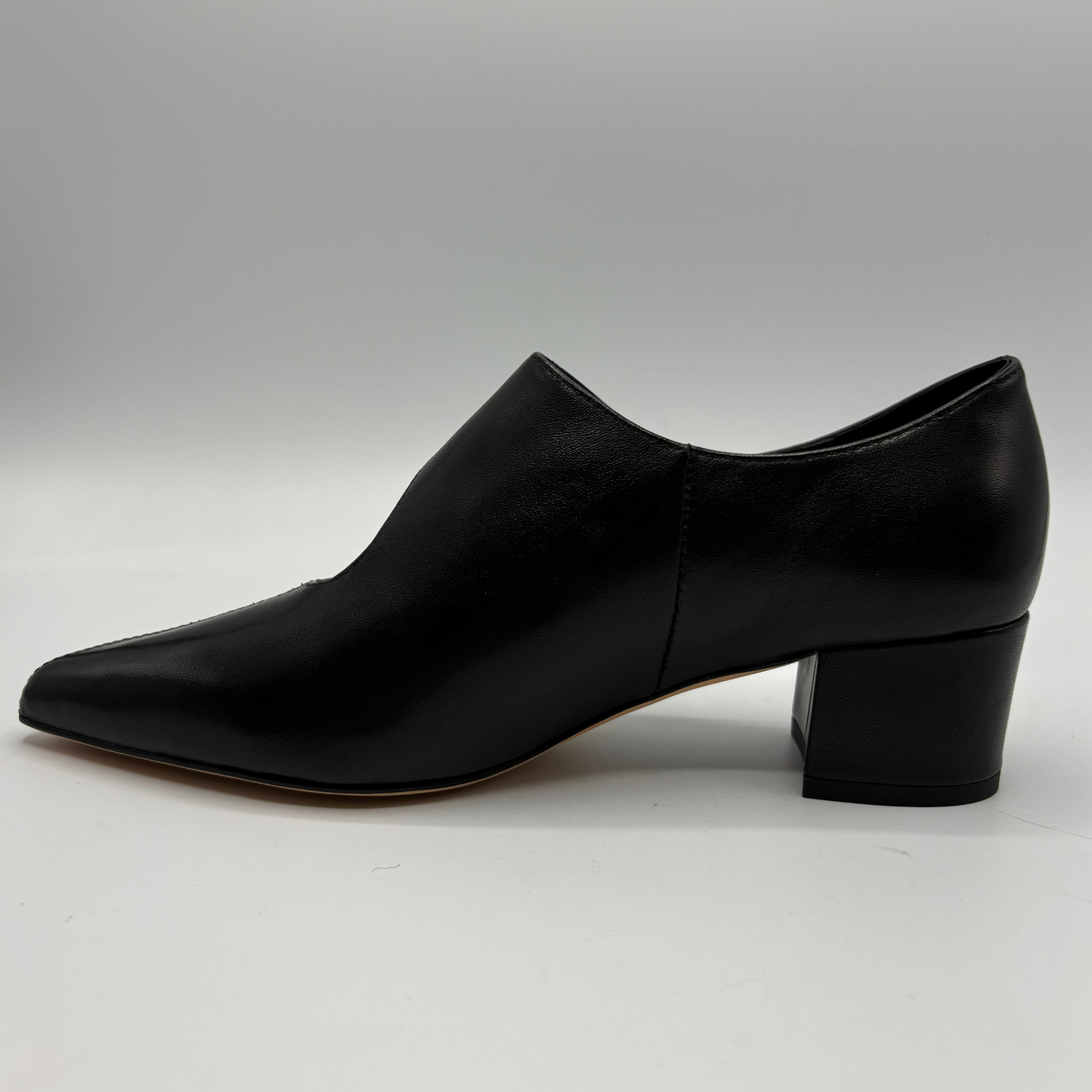 A single black leather pointed-toe heeled shoe shown in side profile against a neutral gray studio background.