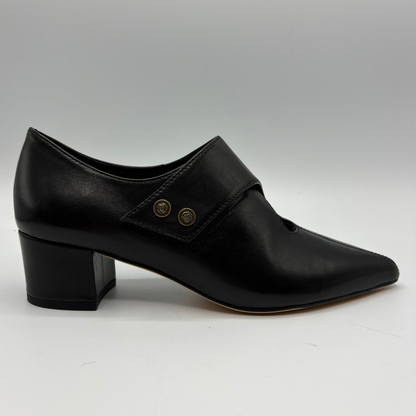 A single black leather low block-heel shoe with a pointed toe and two gold-tone decorative buttons on the side, shown against a neutral gray background.