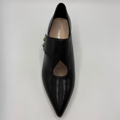 A single black leather pointed-toe flat shoe with a wrap-around strap and two small gold-tone decorative studs, photographed from a top-down angle on a light gray background.