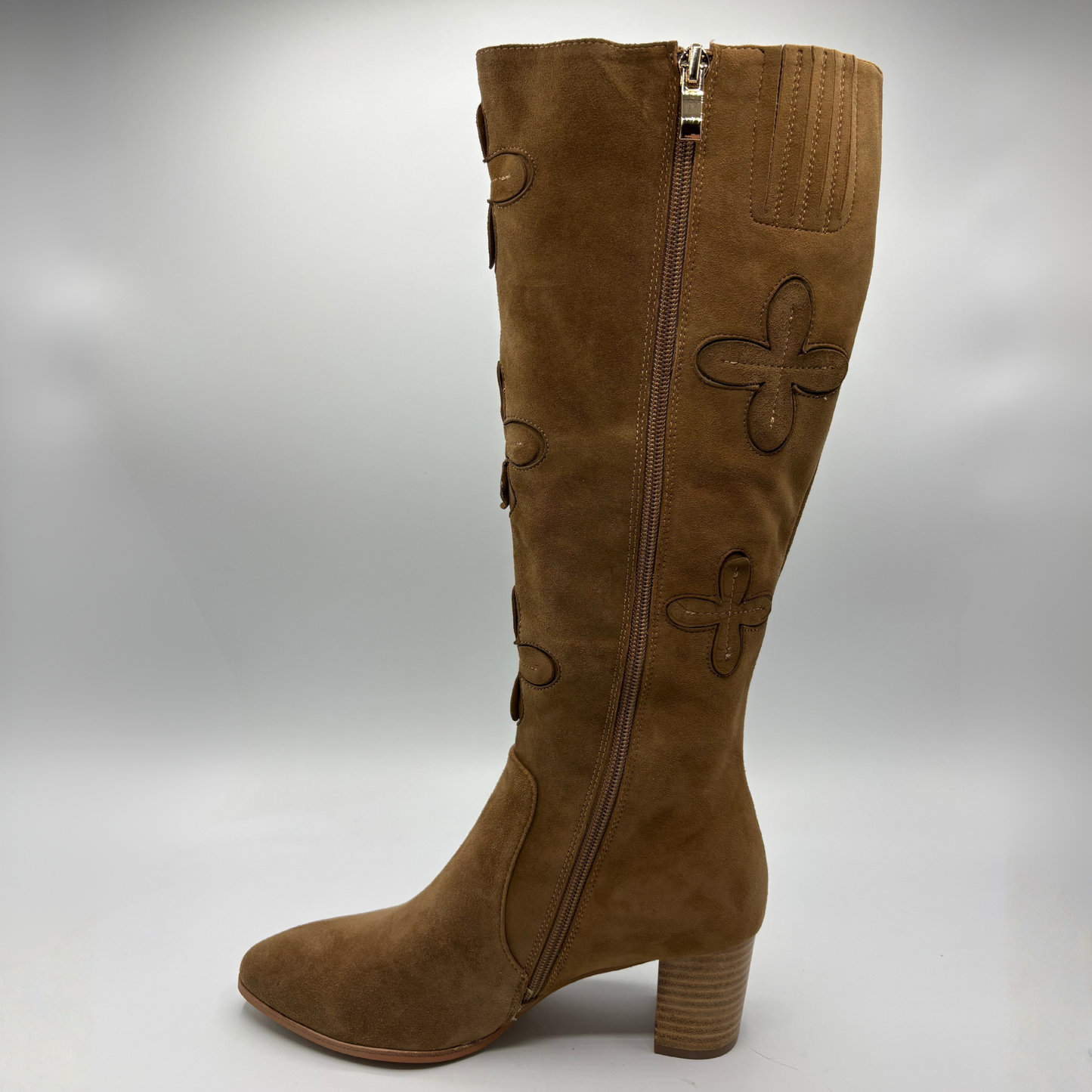 A brown suede knee-high boot with a block heel, side zipper, and decorative stitched clover motifs on the shaft, shown against a neutral gray background.