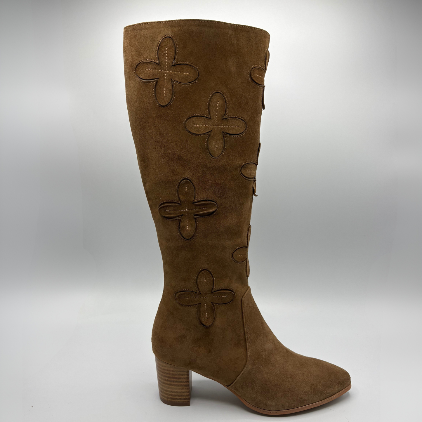 A brown suede knee-high boot with a block heel and decorative stitched clover motifs on the shaft, shown against a neutral gray background.