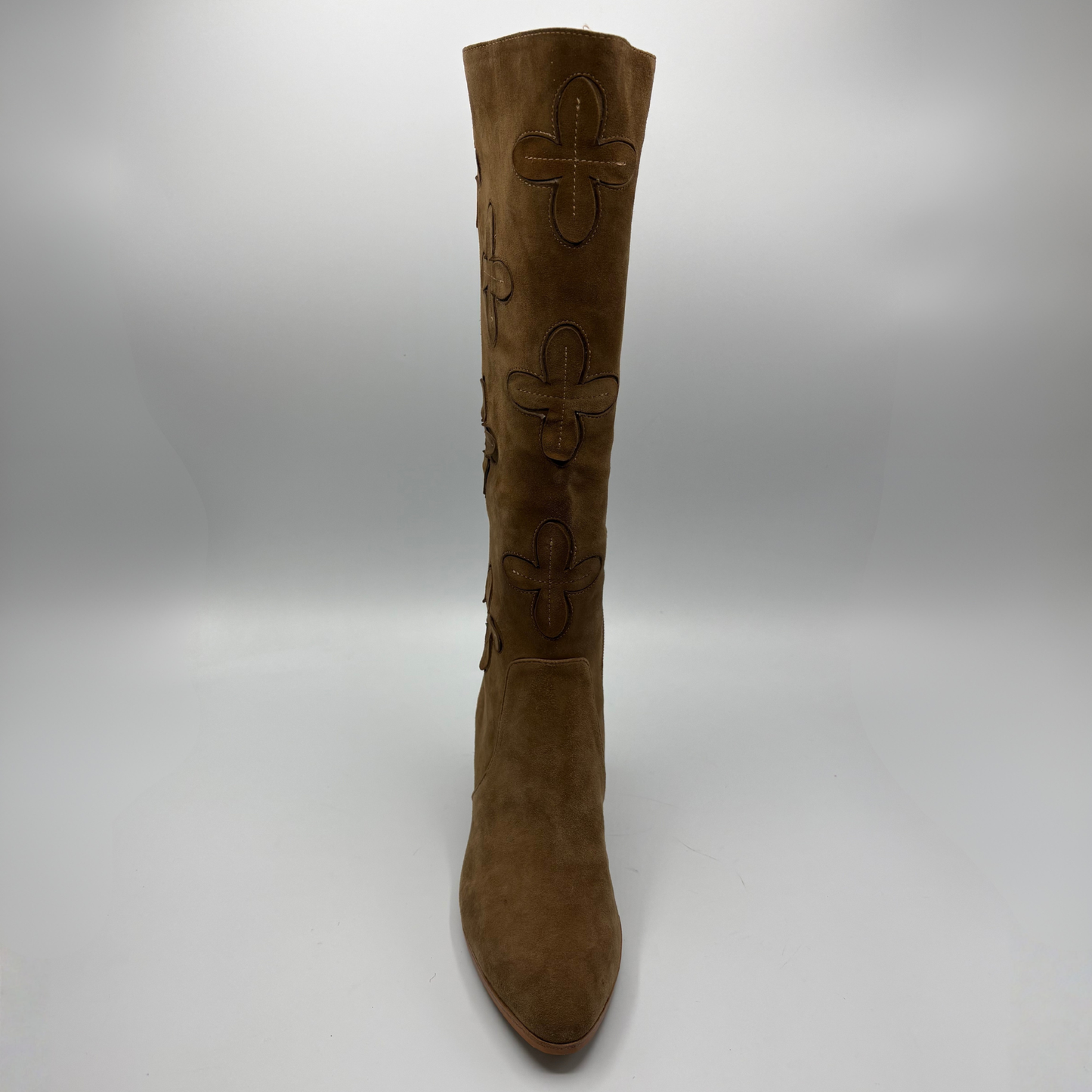 A single knee-high brown suede boot with embossed floral motifs on the shaft, shown against a neutral gray studio background.