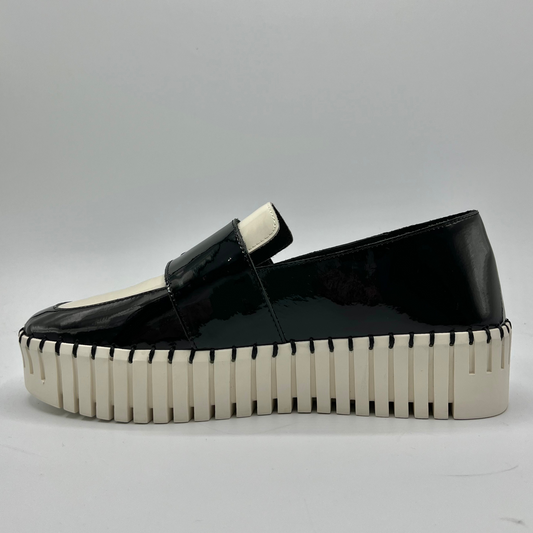 Black patent leather loafer with a thick white sole on a gray background