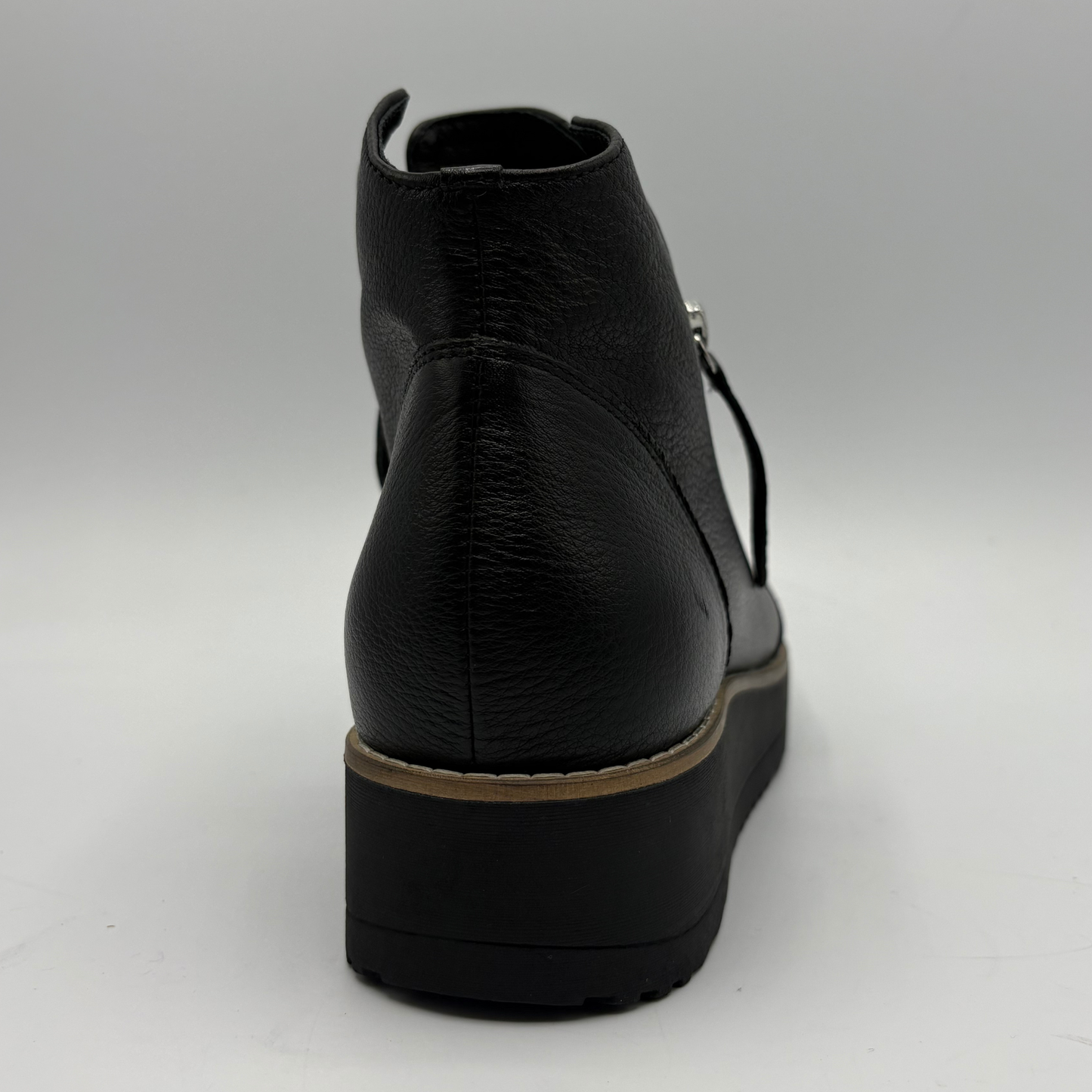 A black leather ankle boot with a chunky platform sole, shown from a rear three-quarter angle against a neutral gray background.