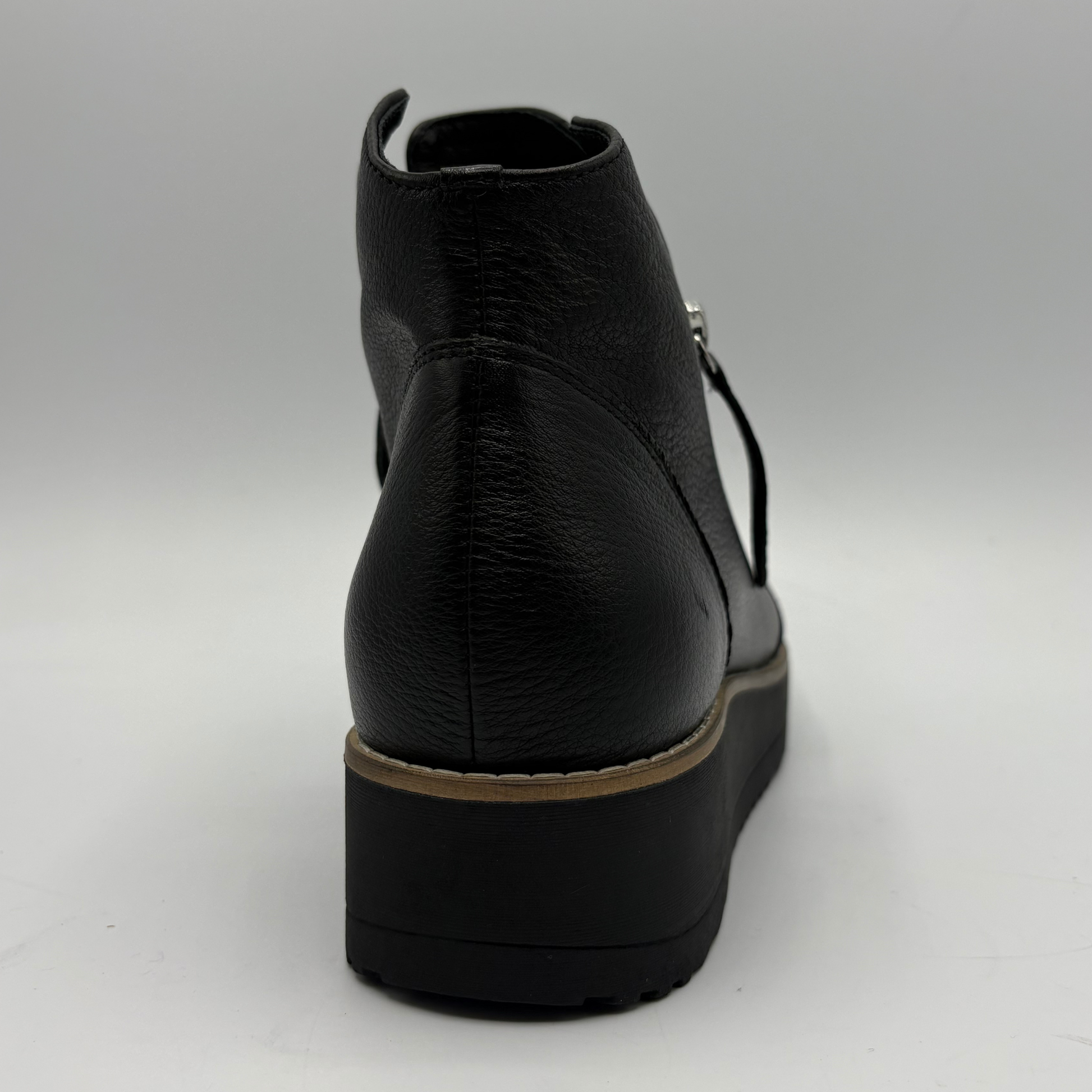 A black leather ankle boot with a chunky platform sole, shown from a rear three-quarter angle against a neutral gray background.