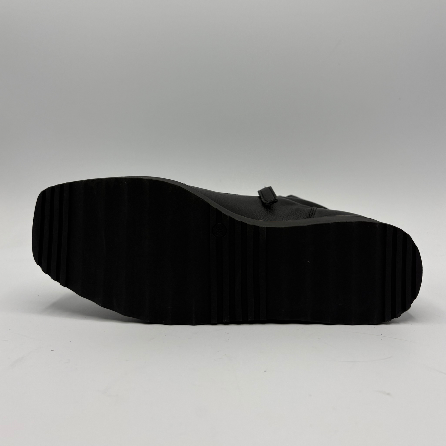 A black leather shoe shown from a side profile view, highlighting its thick, heavily treaded black rubber sole against a light gray studio background.