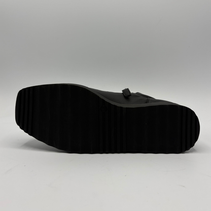 A black leather shoe shown from a side profile view, highlighting its thick, heavily treaded black rubber sole against a light gray studio background.