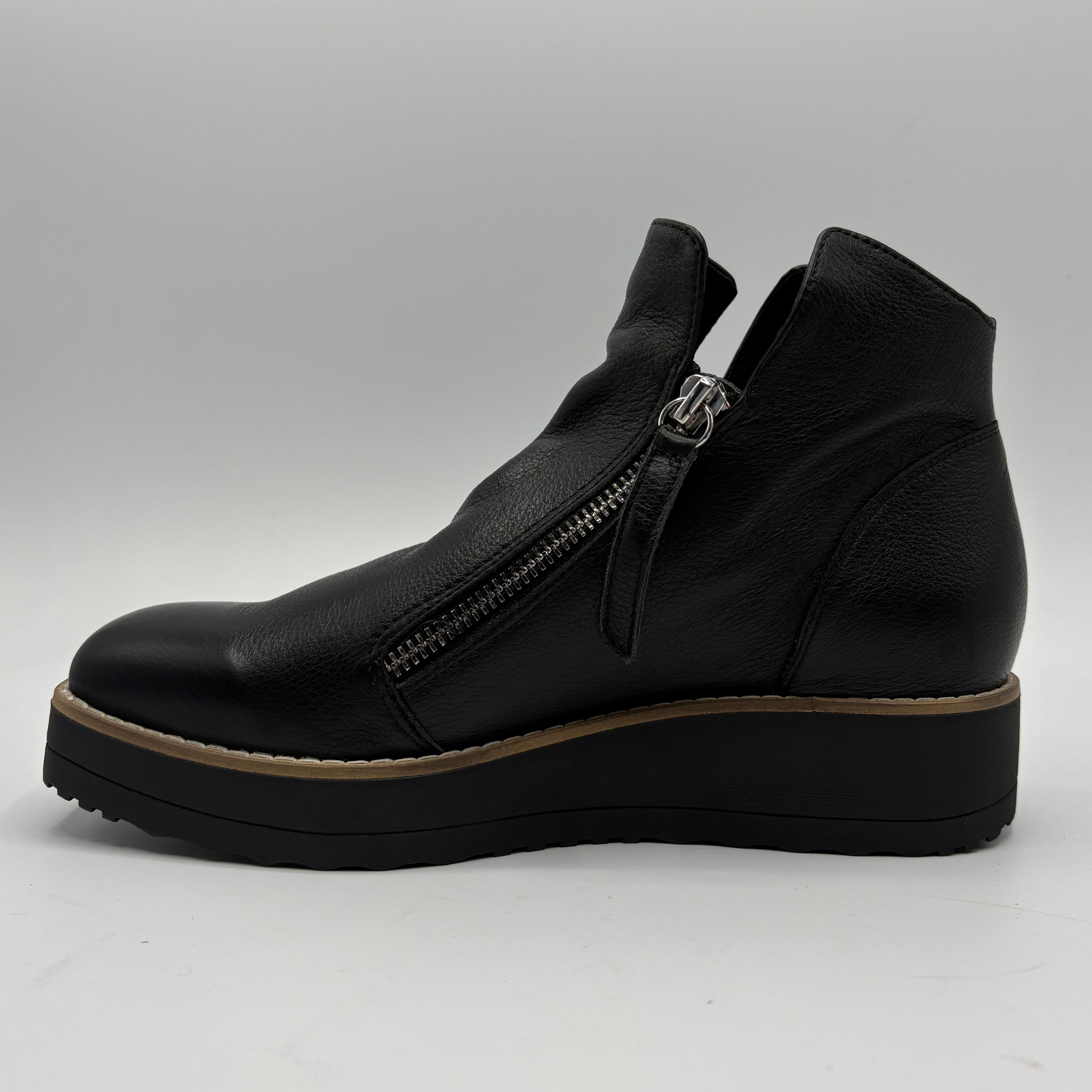 A black leather ankle boot with a side zipper, a chunky black platform sole, and a tan midsole stripe, shown from a side profile view against a light gray background.