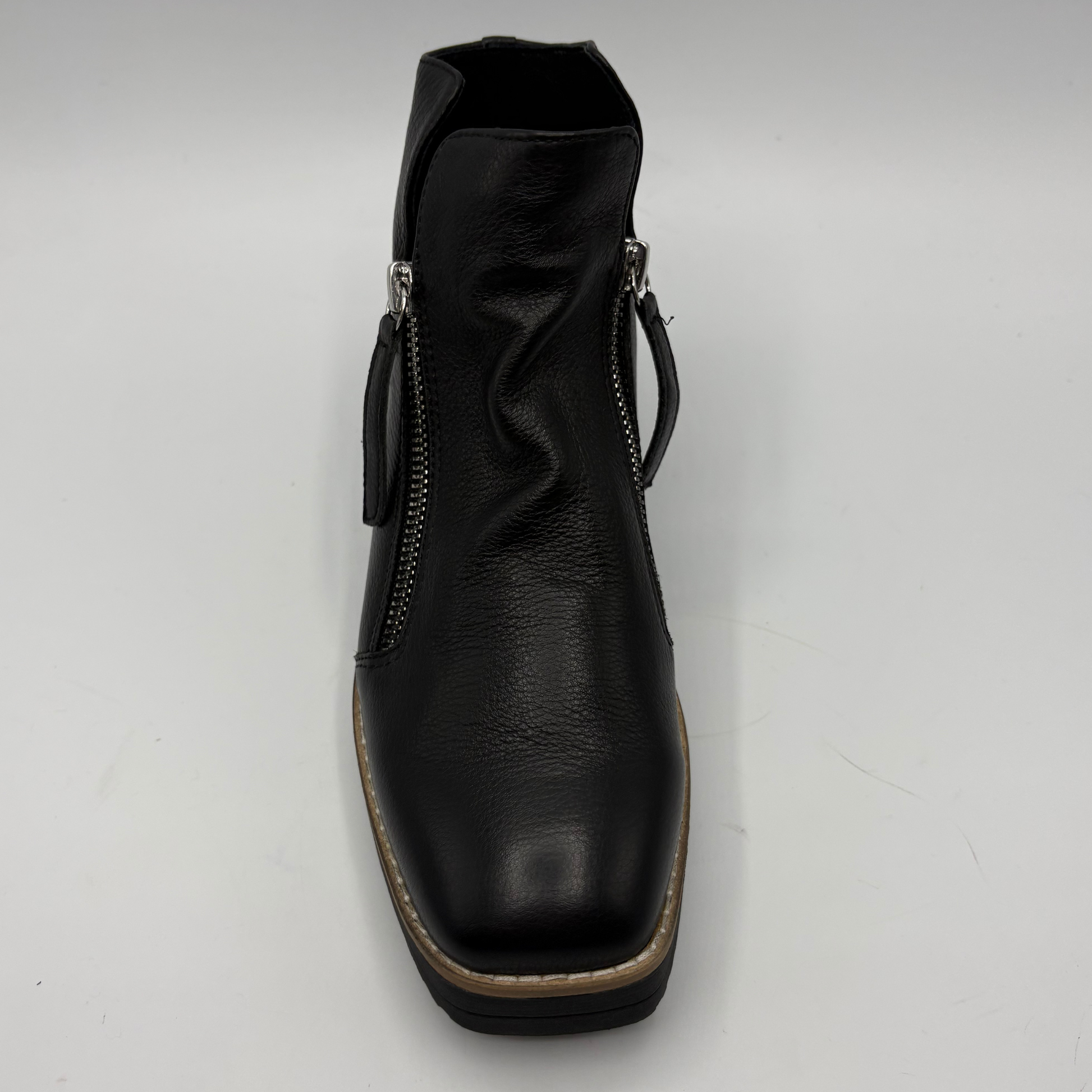 A black leather ankle boot with side zippers, a low block heel, and a tan outsole, shown from a top-down view on a white background.
