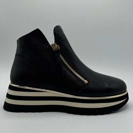 Black platform sneaker with a gold zipper on a grey background