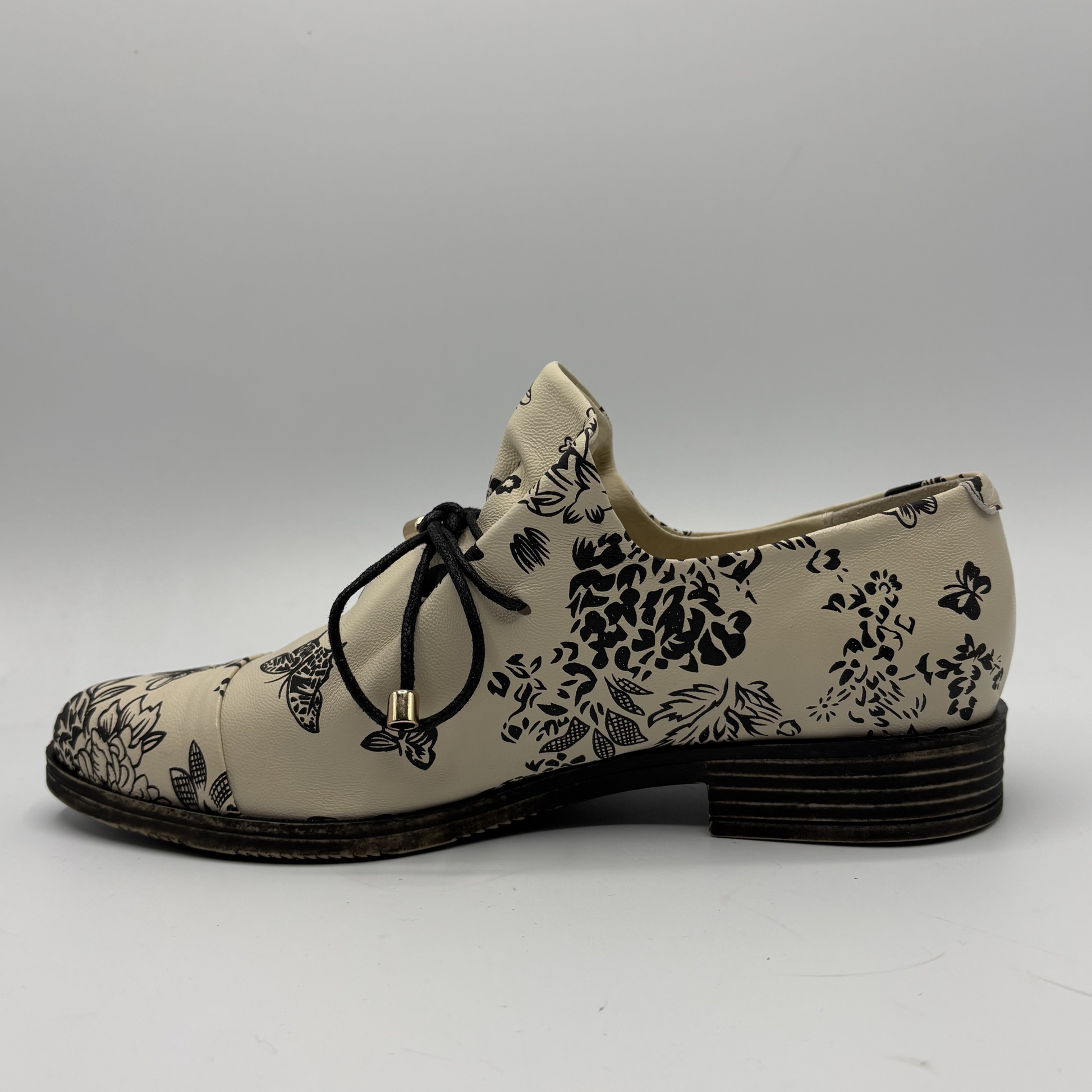 Beige shoe with black floral pattern on a gray background