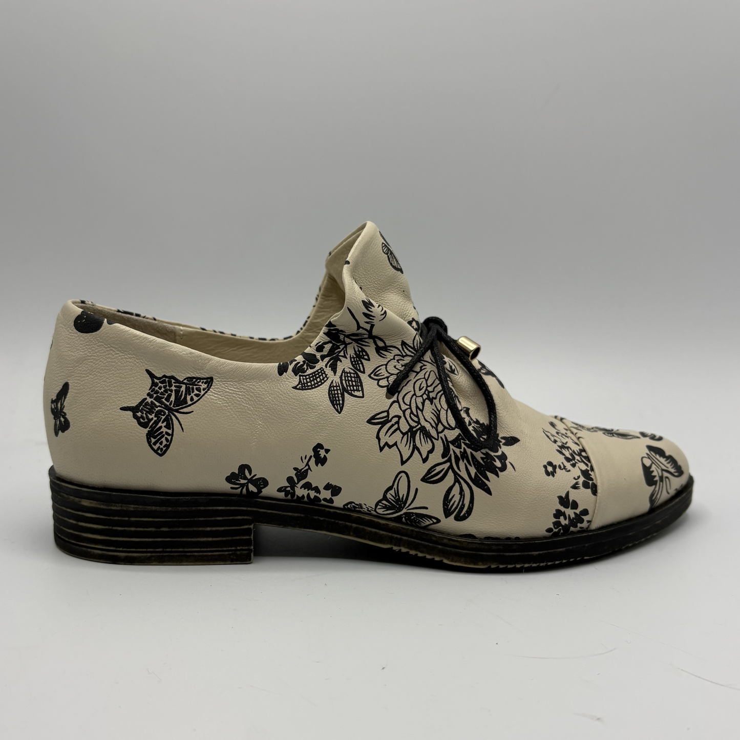 Beige shoe with black floral pattern on a white background