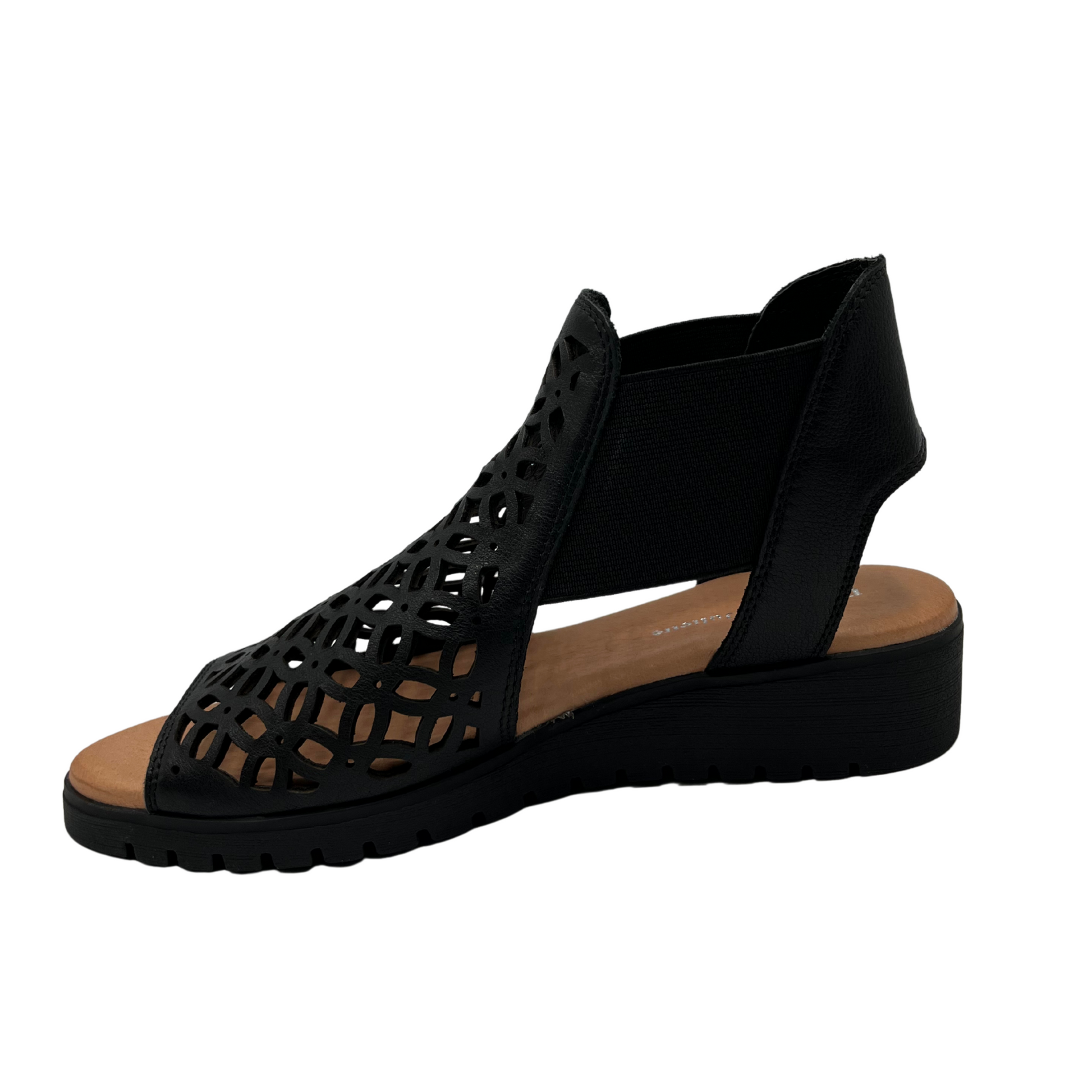 Left view of leather die cut wedge sandal in black. Low wedge heel, elasticized sides and open toe 