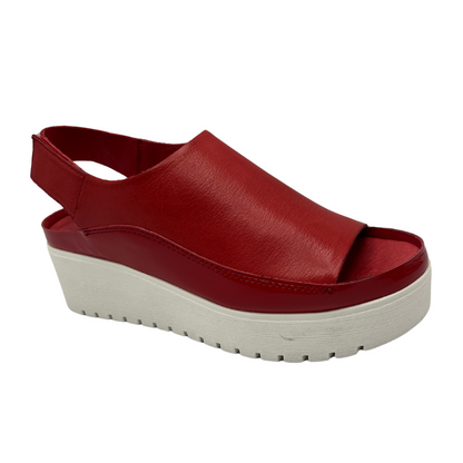 Angled view of red leather sandal with white rubber outsole. Velcro slingback strap and rounded toe.