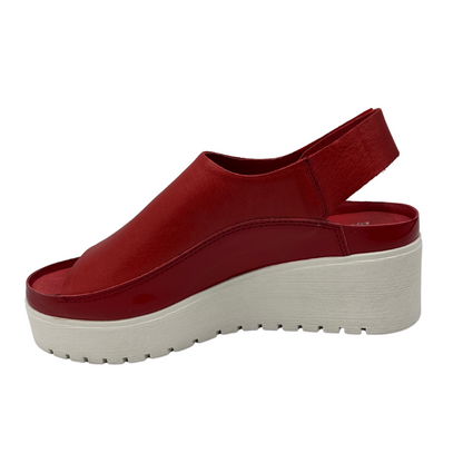 Left view of red leather sandal with white rubber outsole. Velcro slingback strap and rounded toe.