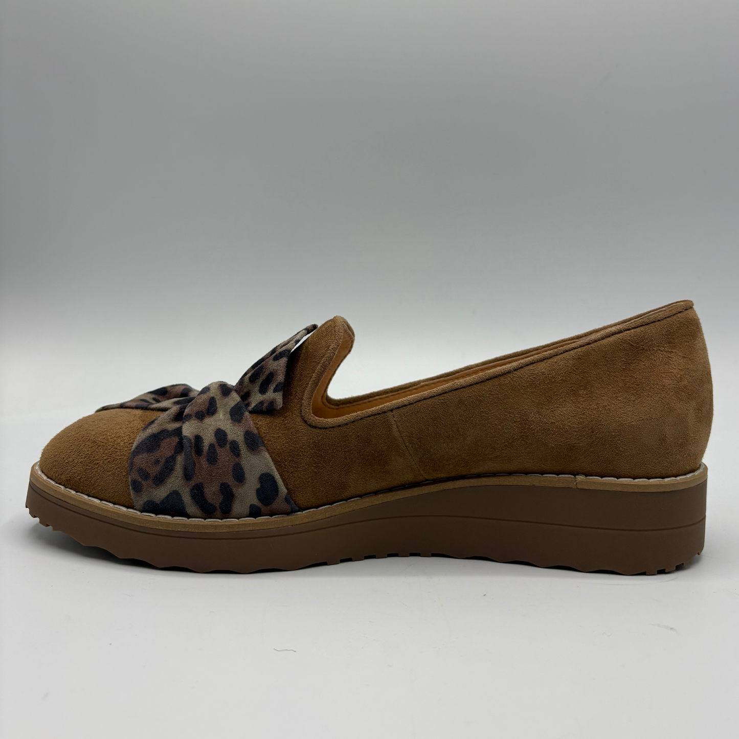 A single women's slip-on wedge shoe in brown suede with a leopard-print fabric bow across the vamp, shown in profile against a neutral gray background.