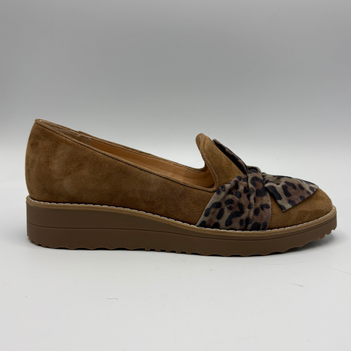 A single women's slip-on wedge shoe in brown suede with a leopard-print fabric bow detail across the vamp, shown in profile against a neutral gray background.