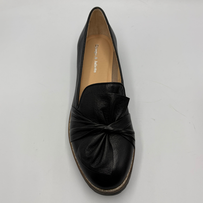 A single black leather slip-on loafer with a gathered bow detail on the toe, photographed from a top-down angle on a light gray background.