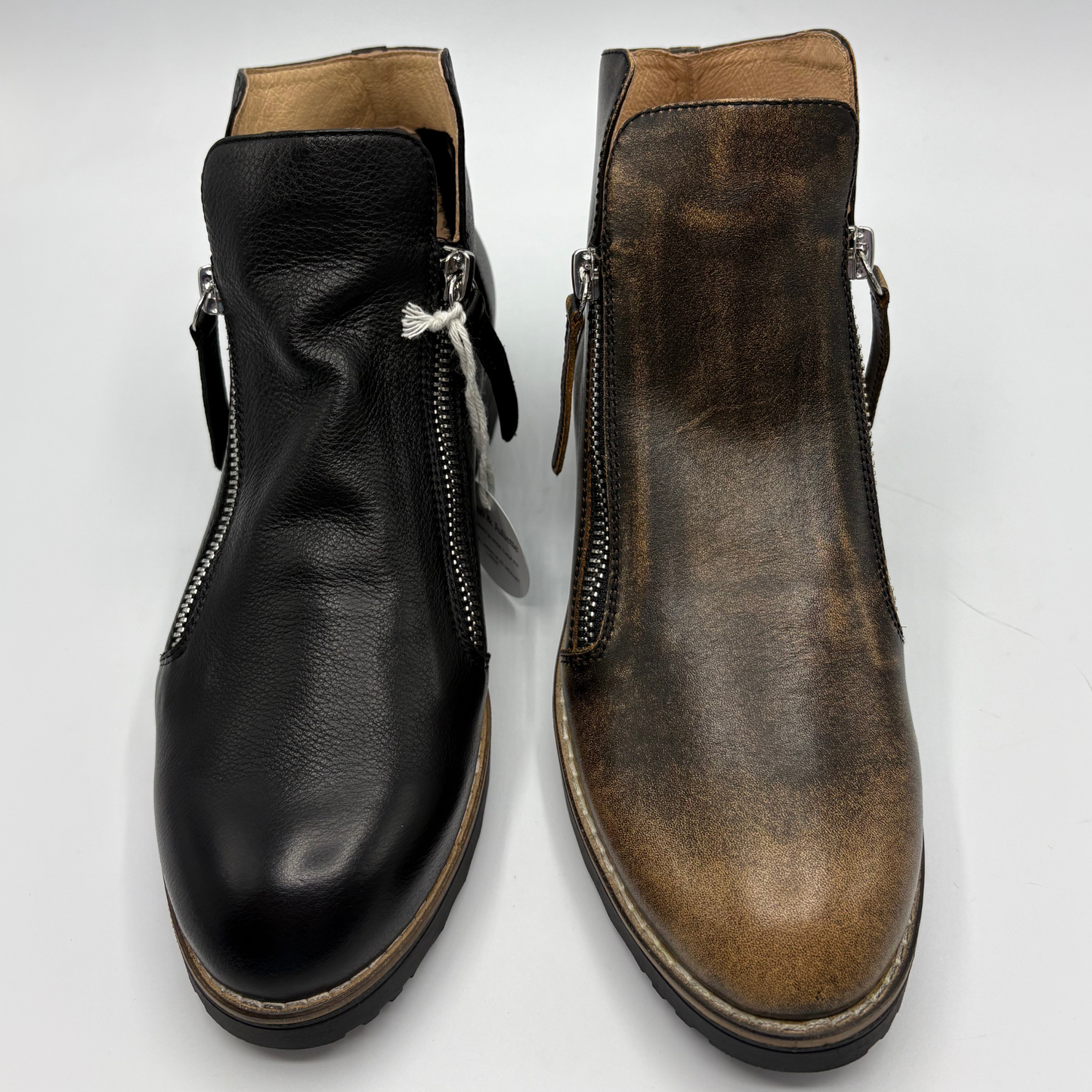 A pair of ankle boots shown side by side on a white background, one in smooth black leather and the other in distressed brown leather, both with side zippers.