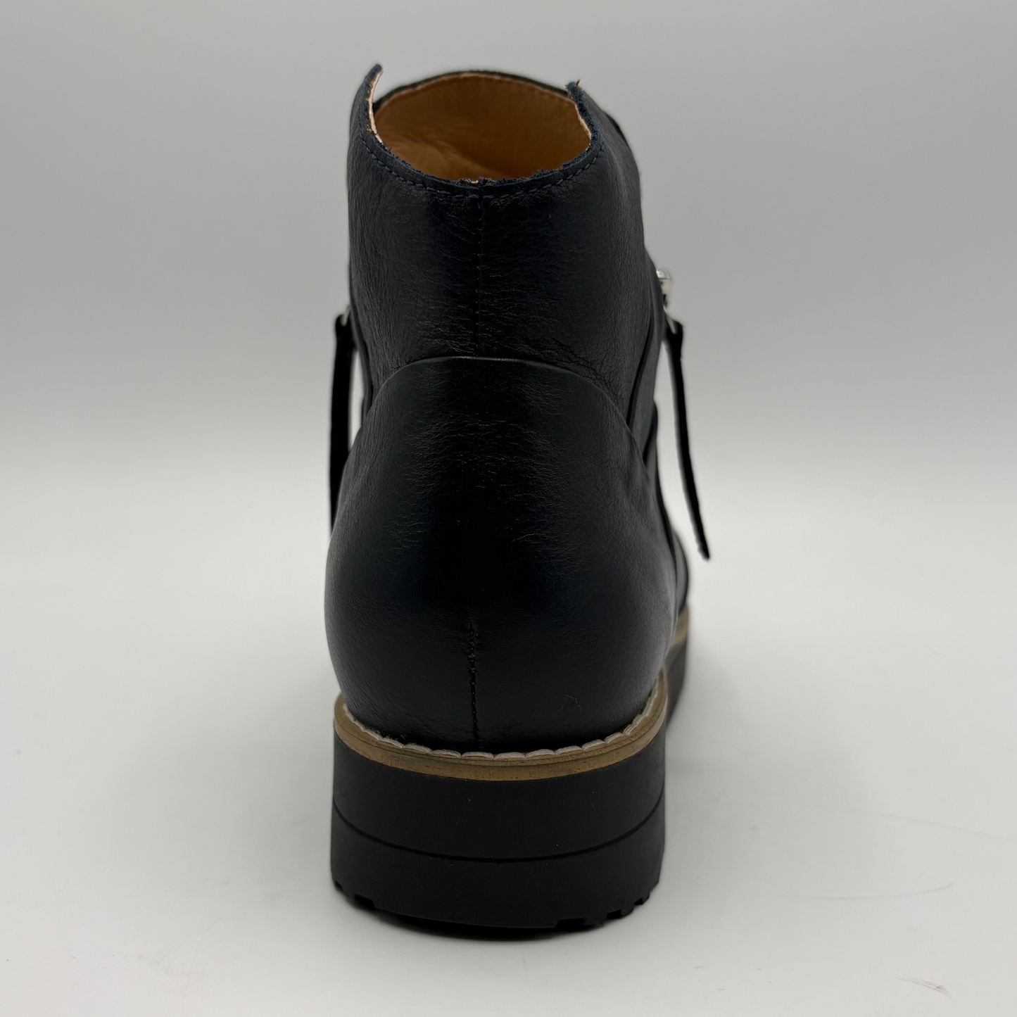A black leather ankle boot shown from the back, featuring a chunky black sole with a tan midsole stripe and a tan interior lining, set against a plain light gray background.