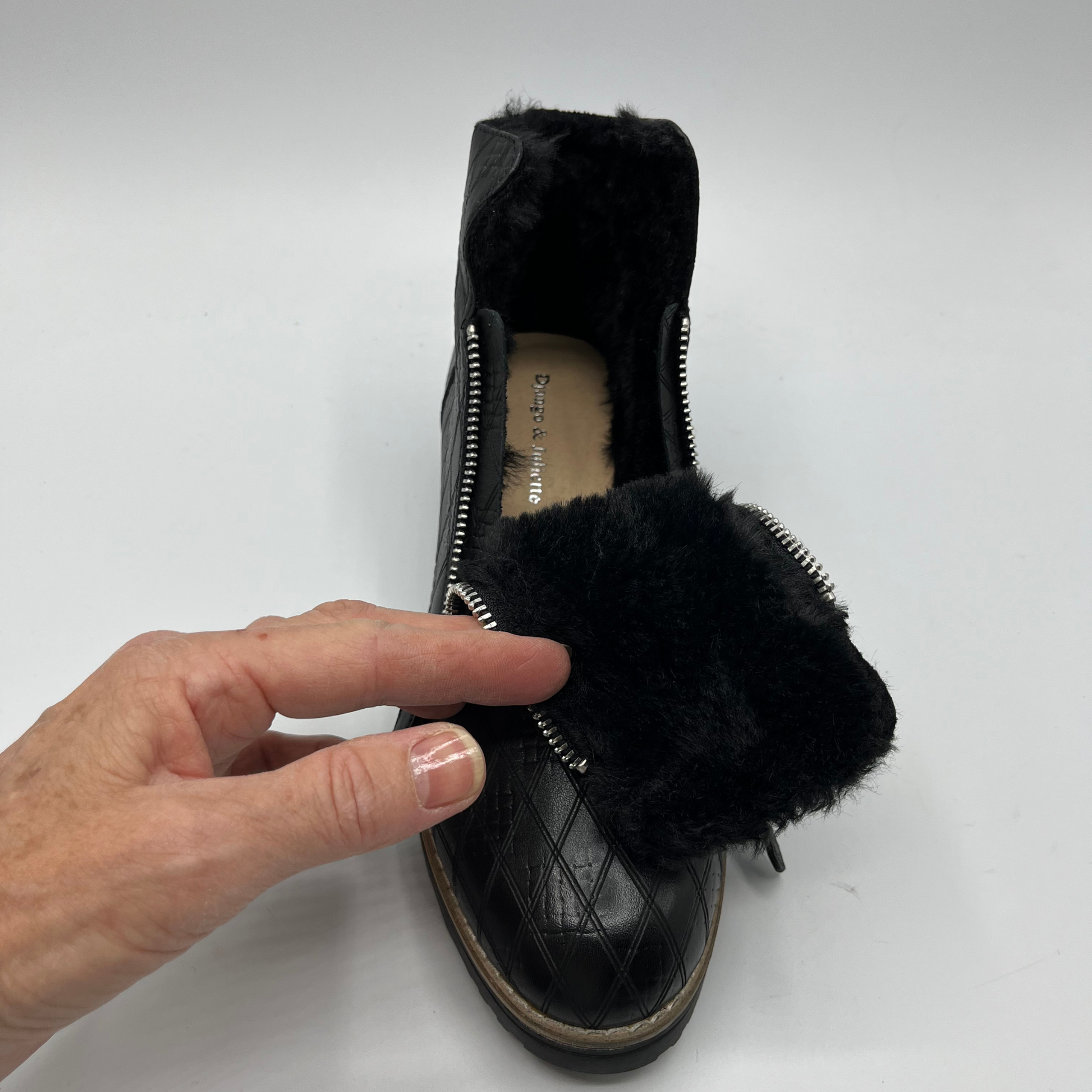 Black short boot with a faux fur lining held by a hand on a white background