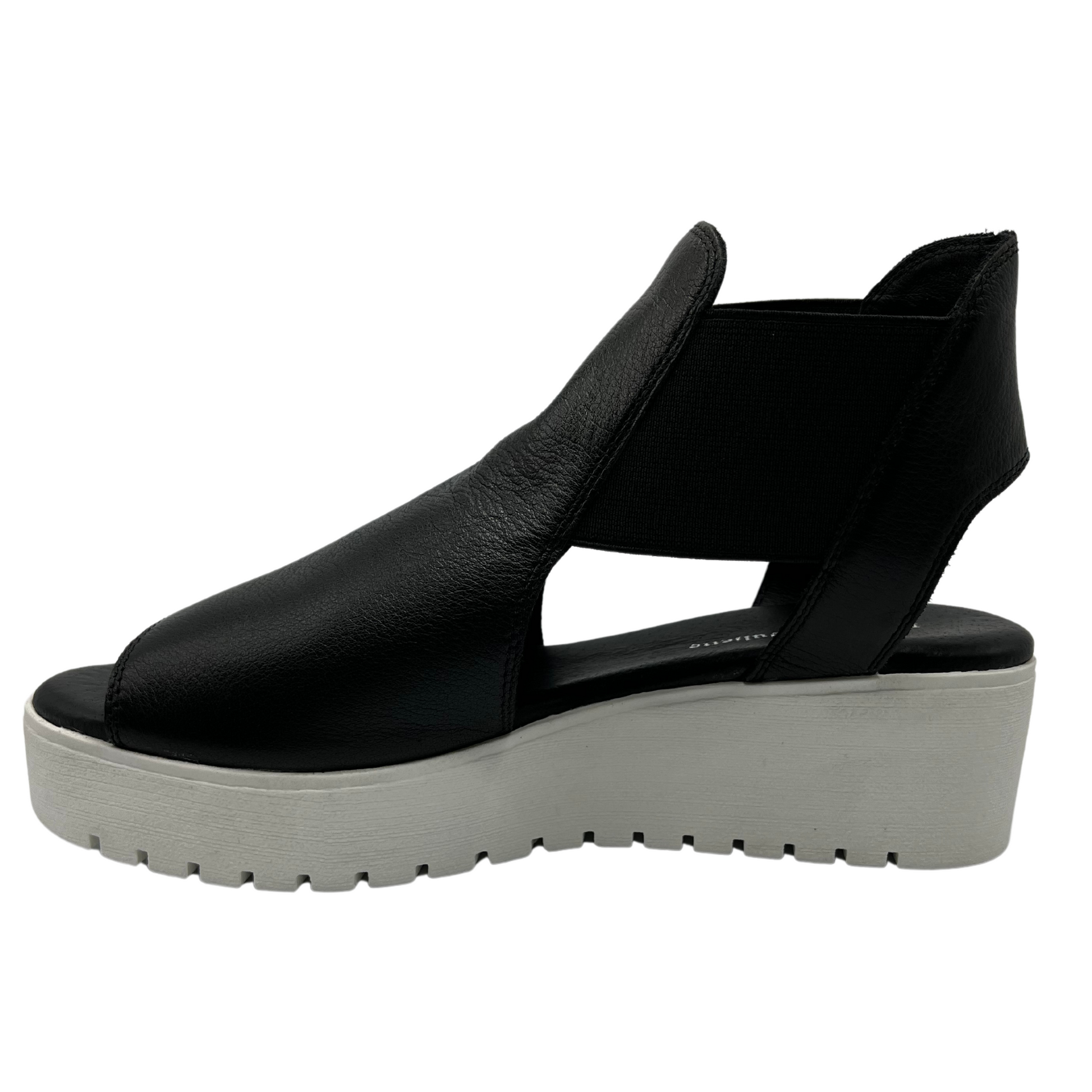 Left facing view of black leather sandal with elastic side straps and low wedge heel