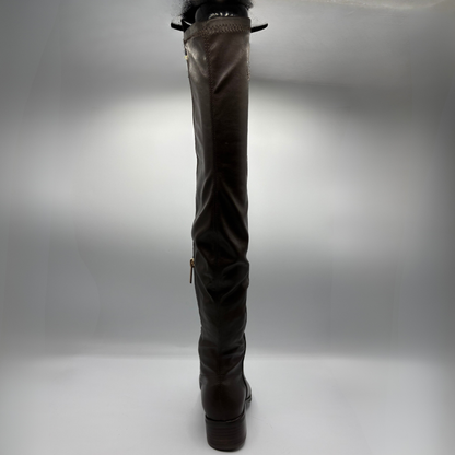 A single dark brown leather over-the-knee boot shown from the back, featuring a low block heel, side zipper, and a black bow detail at the top, set against a neutral gray studio background.