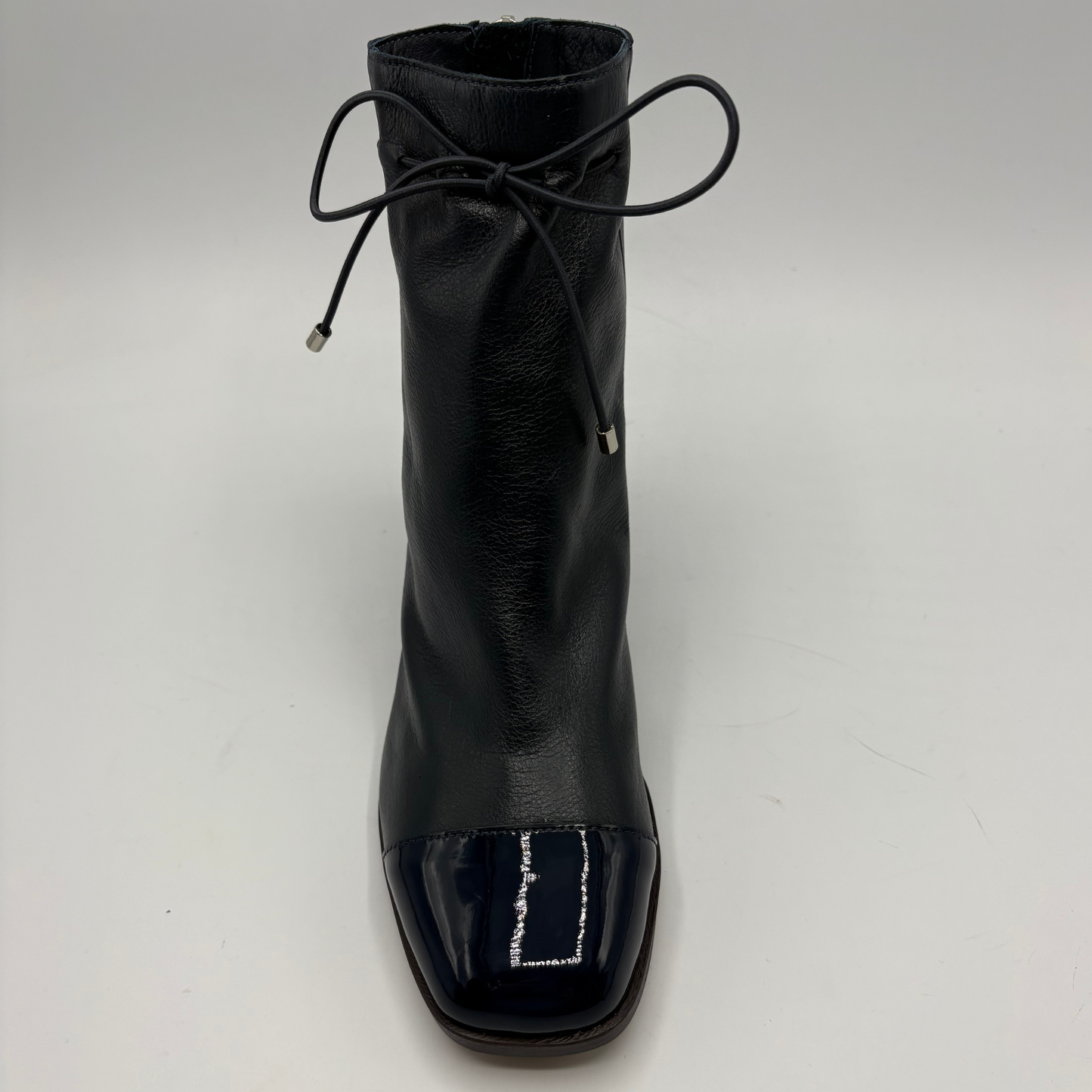 A single navy leather ankle boot with a glossy patent leather toe cap and a thin black lace tied at the collar, shown against a plain light gray background.