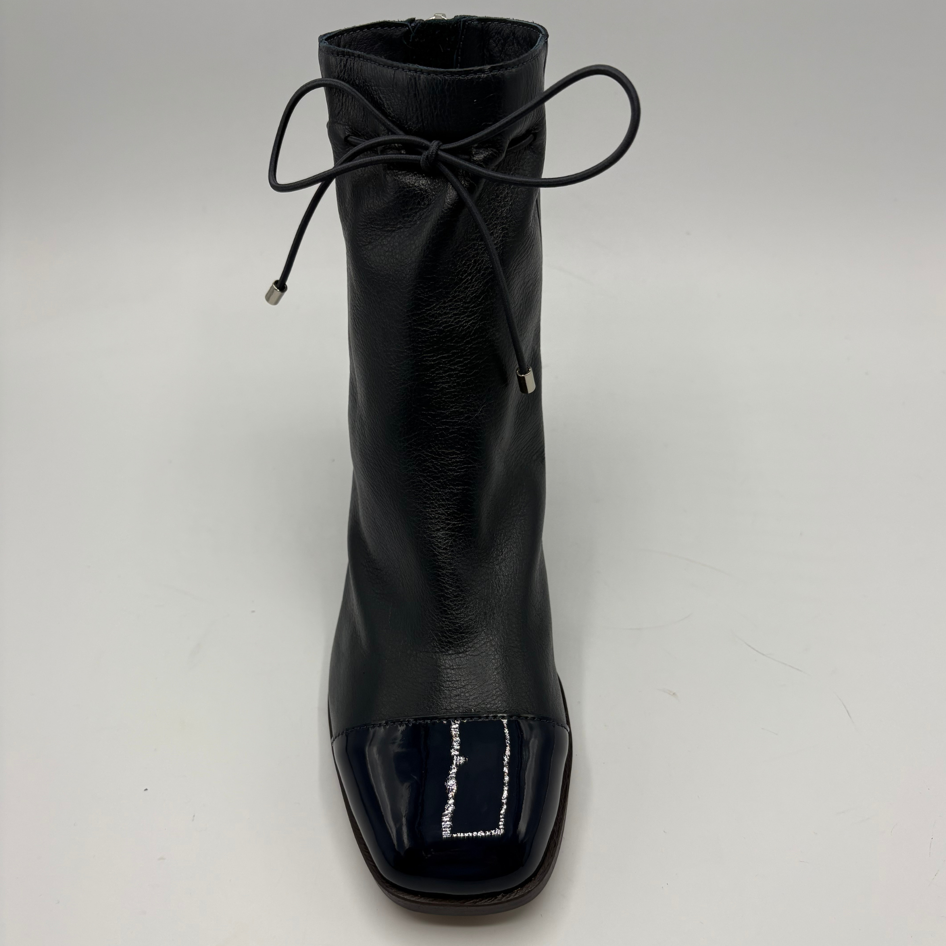 A single navy leather ankle boot with a glossy patent leather toe cap and a thin black lace tied at the collar, shown against a plain light gray background.