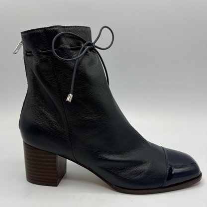 A navy leather ankle boot with a chunky brown block heel, a glossy cap toe, and thin black laces tied at the ankle, shown against a light gray background.