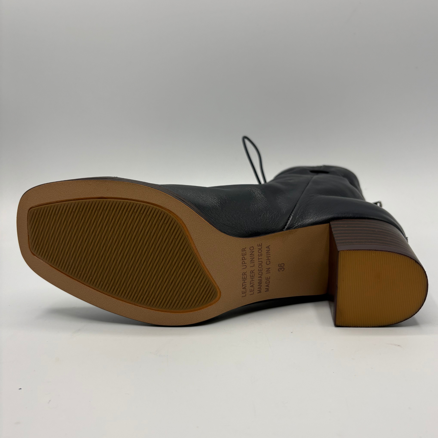 The bottom sole view of a navy leather ankle boot with a brown rubber outsole and block heel, displayed on a light gray background.