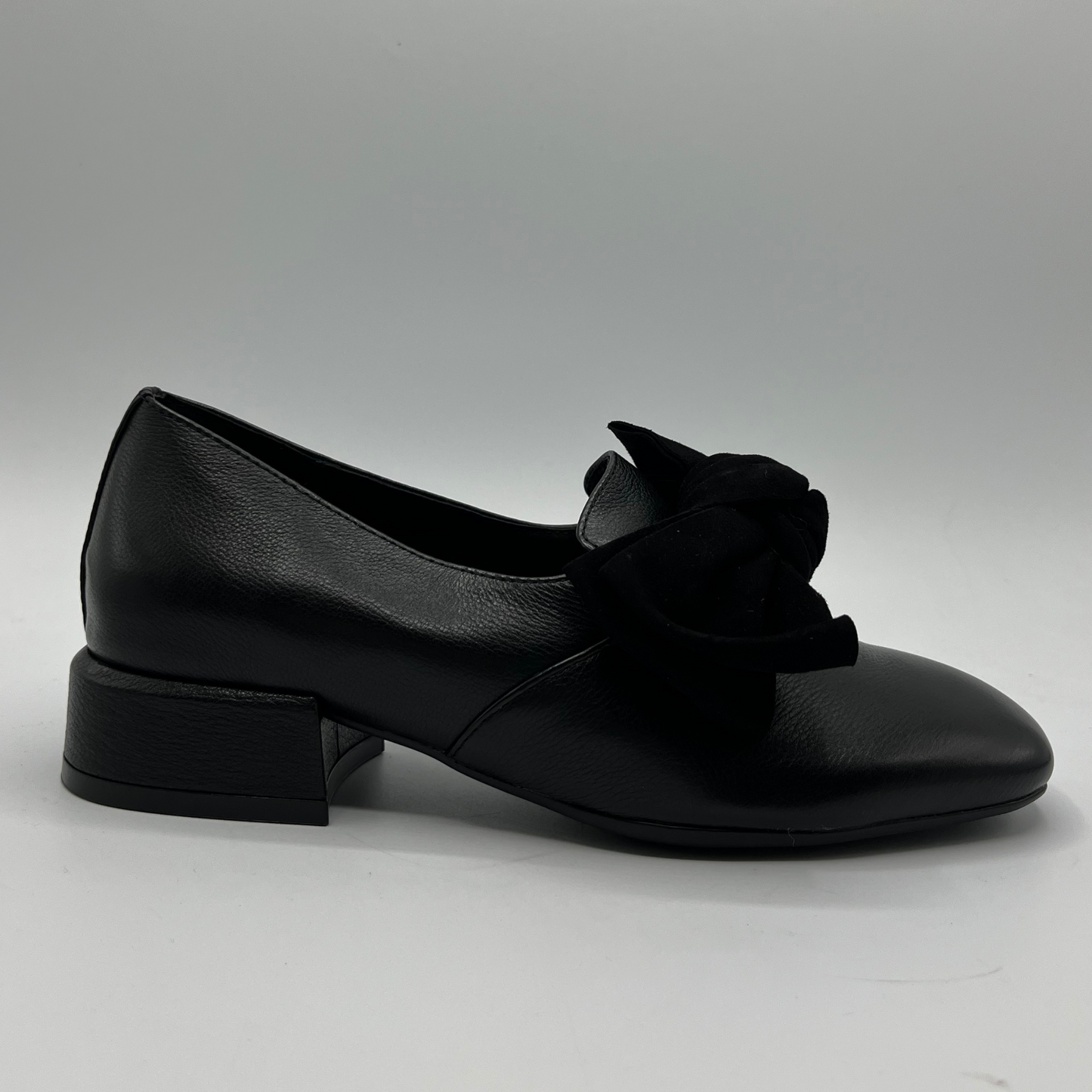 Black leather shoe with a bow on a gray background