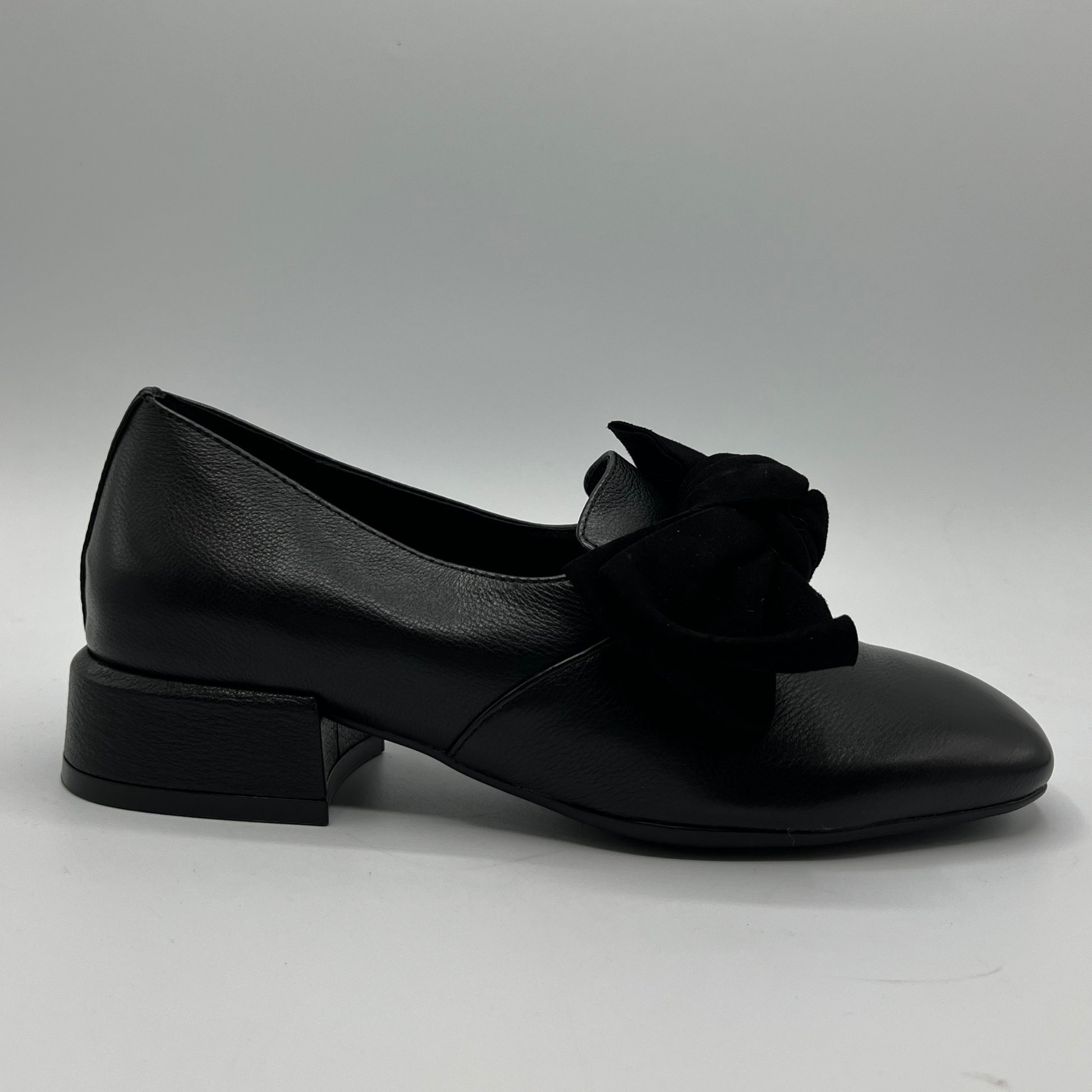 Black leather shoe with a bow on a gray background