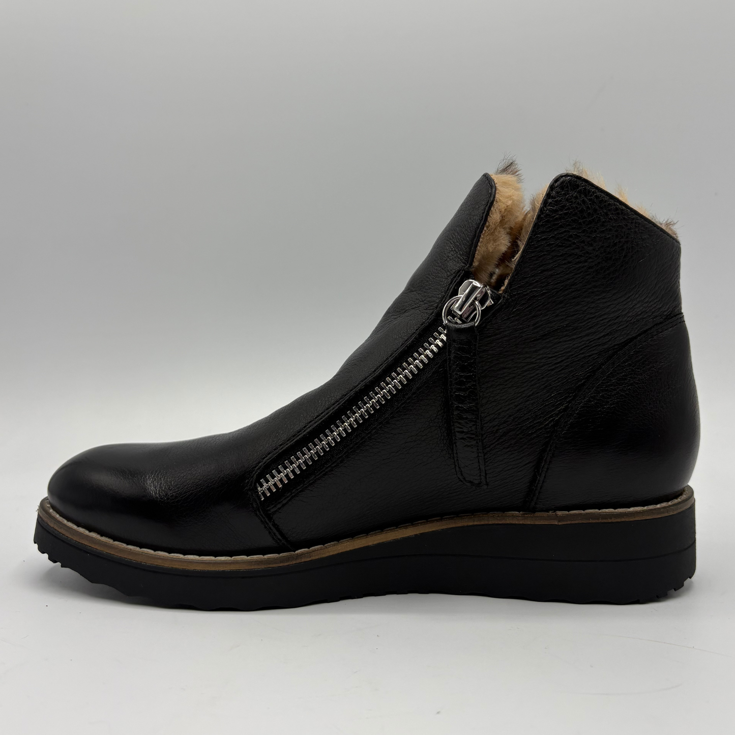 A black leather ankle boot with a side zipper, a tan faux-fur lining visible at the collar, and a wedge sole, shown from a side profile on a light gray background.