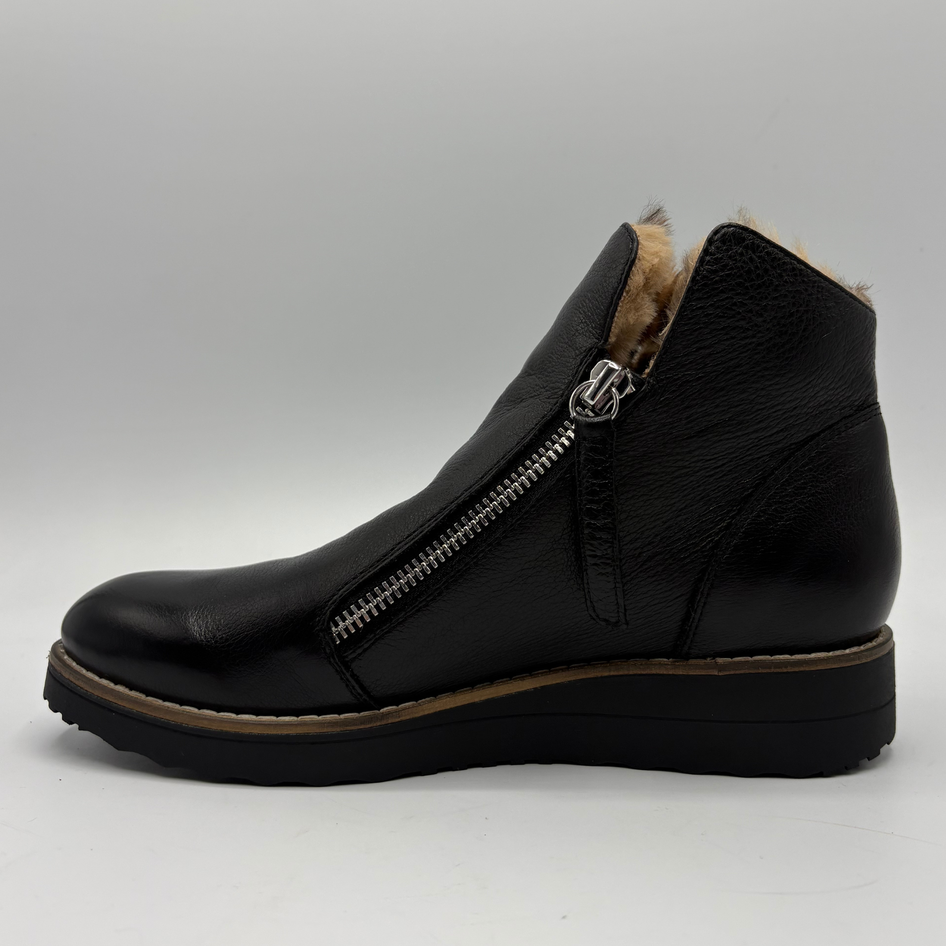 A black leather ankle boot with a side zipper, a tan faux-fur lining visible at the collar, and a wedge sole, shown from a side profile on a light gray background.