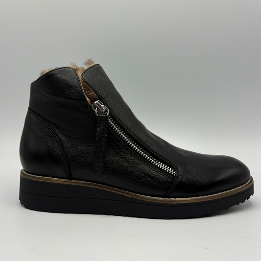A black leather ankle boot with a side zipper, brown faux-fur lining, and a chunky black wedge sole, shown from a side profile on a light gray background.