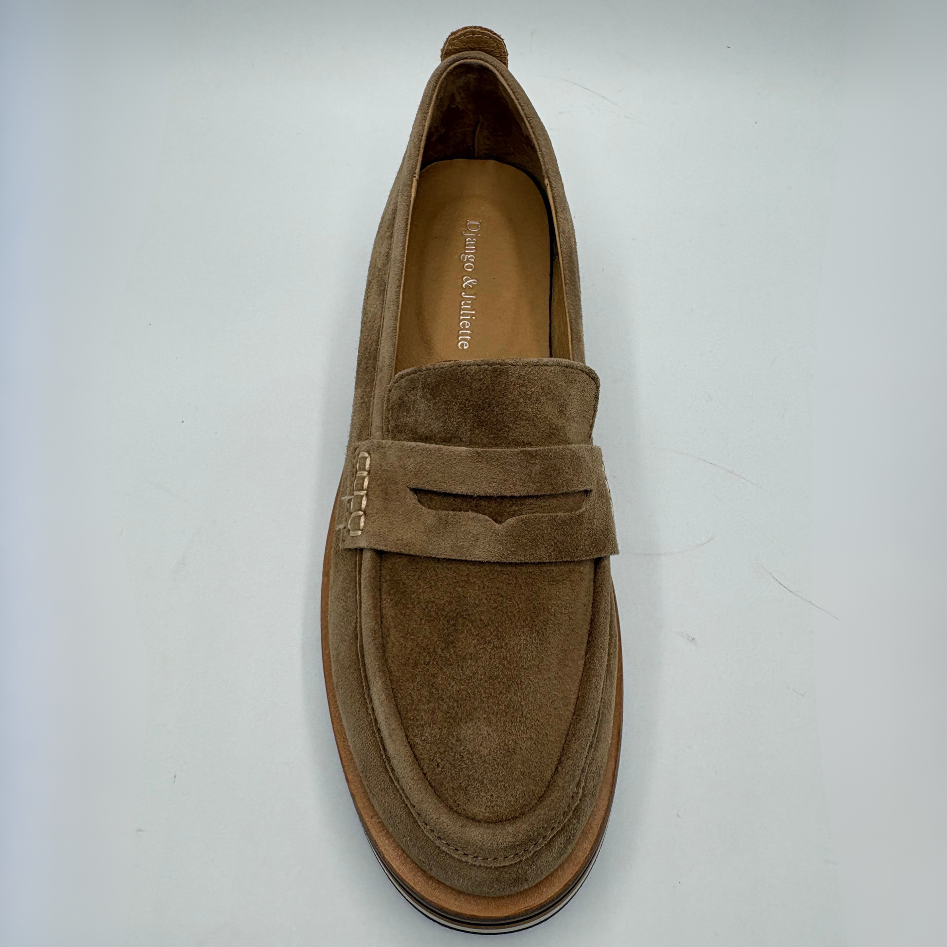 A single brown suede penny loafer shown from a top-down view on a light gray background. The shoe features a wide strap with decorative stitching and a low platform sole.