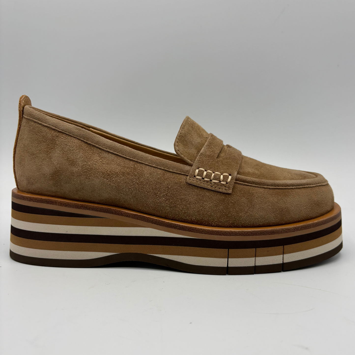 A single brown suede platform loafer with a stacked multi-colored platform sole and a small gold-tone chain detail on the strap, shown against a neutral gray background.