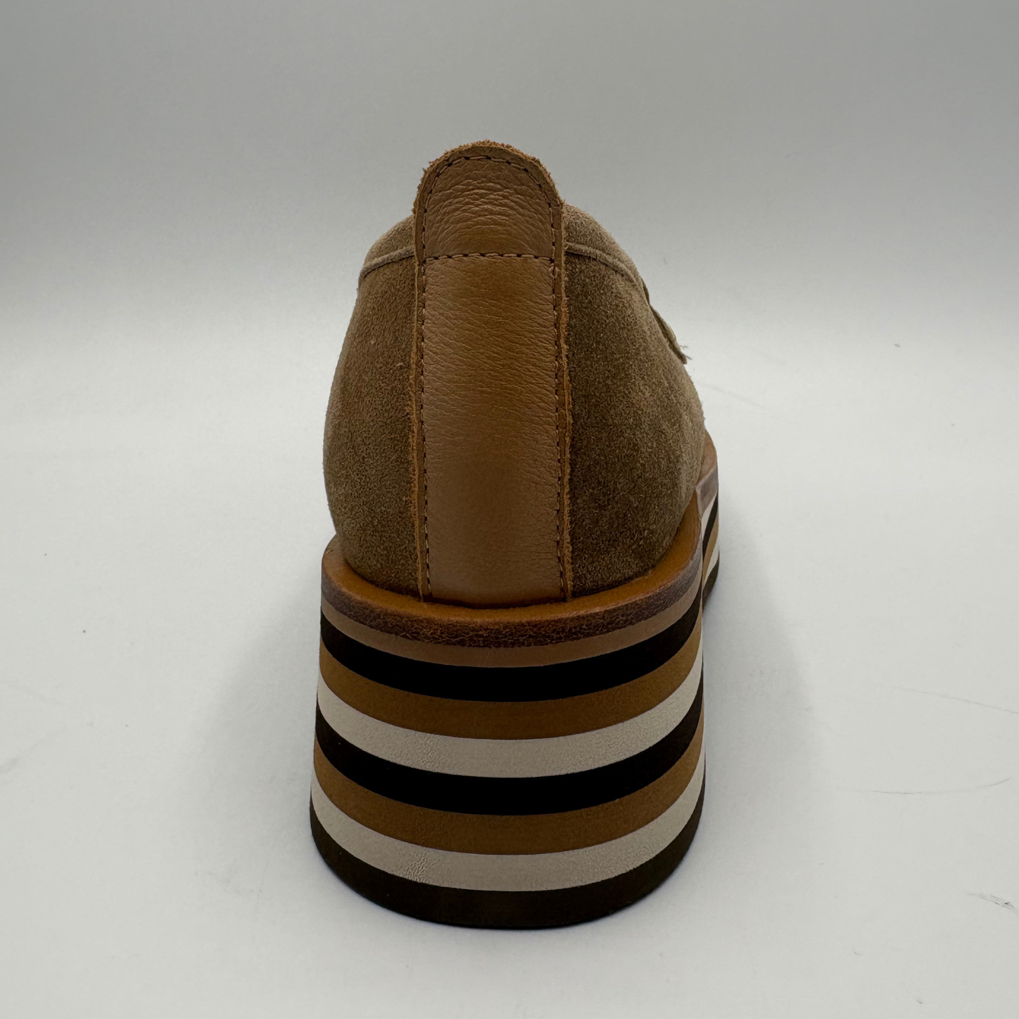 A brown suede and leather loafer shown from the back, featuring a chunky striped platform heel in brown, black, and cream.