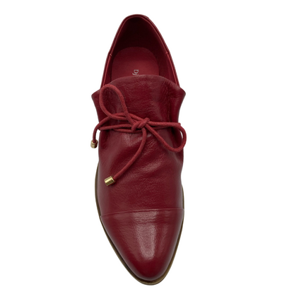 Top view of red leather shoe with pointed toe, red laces and red insoles.