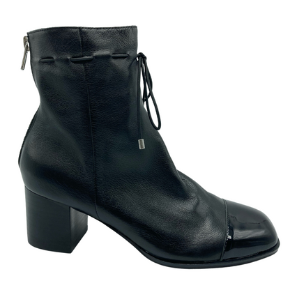 Right facing profile view of black leather ankle boot with skinny tie around ankle. Block heel and silver aglets on laces