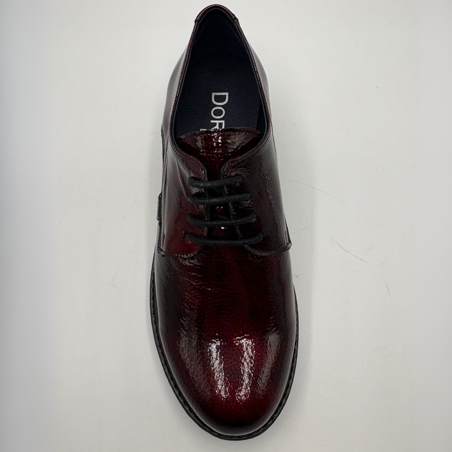 A single men's oxford-style dress shoe in glossy deep burgundy leather with black laces, photographed from above on a plain light background. The insole shows the brand name 'DORKING’
